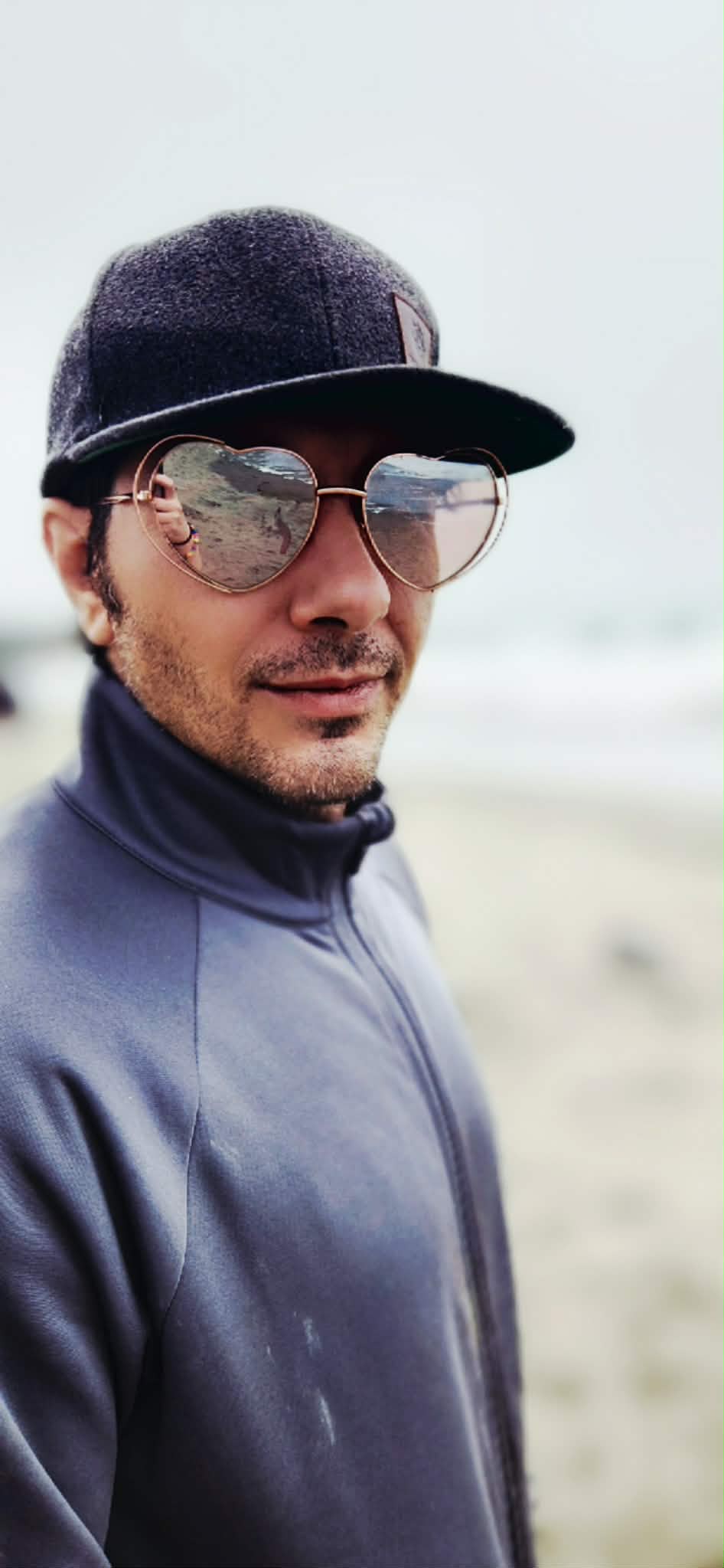 Elijah, founder of Logos & Telos, on the beach in a cap and sunglasses