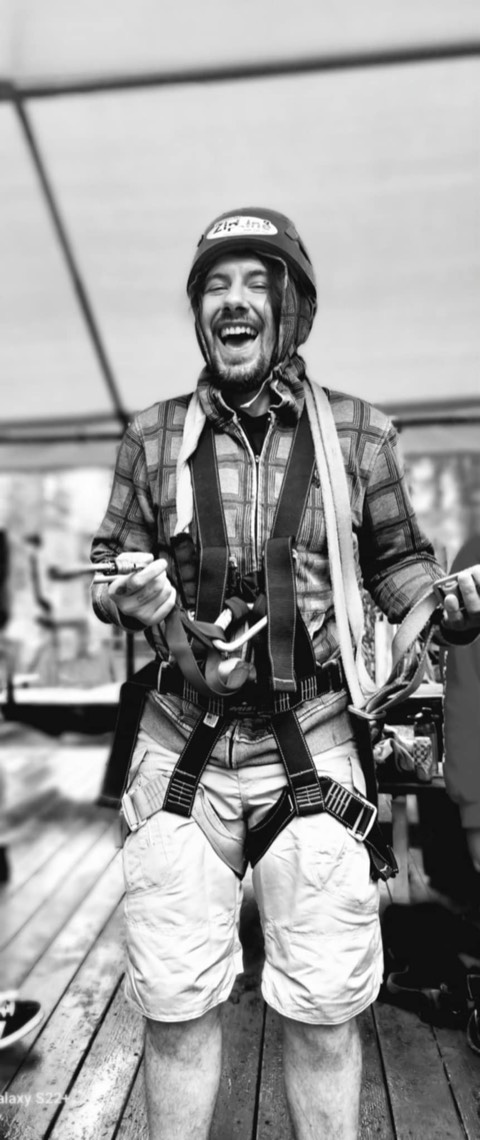 Elijah laughing in a climbing helmet and harness, in black and white