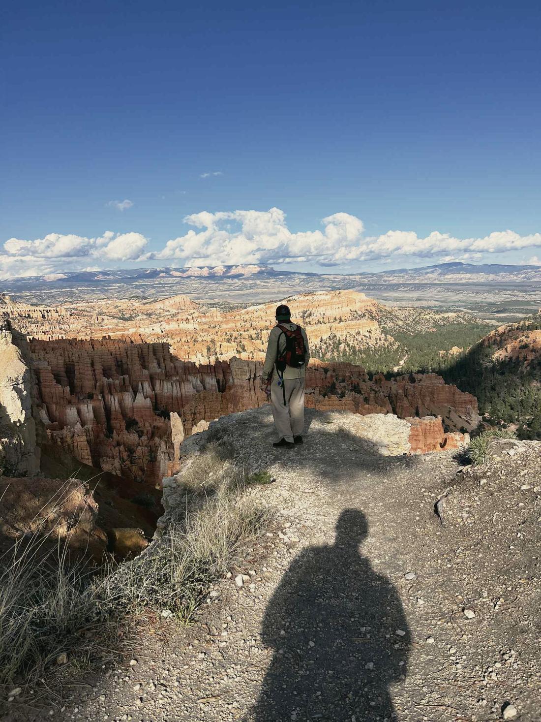 A hiker at the edge of a canyon rim, the photographer's shadow stretched across the trail