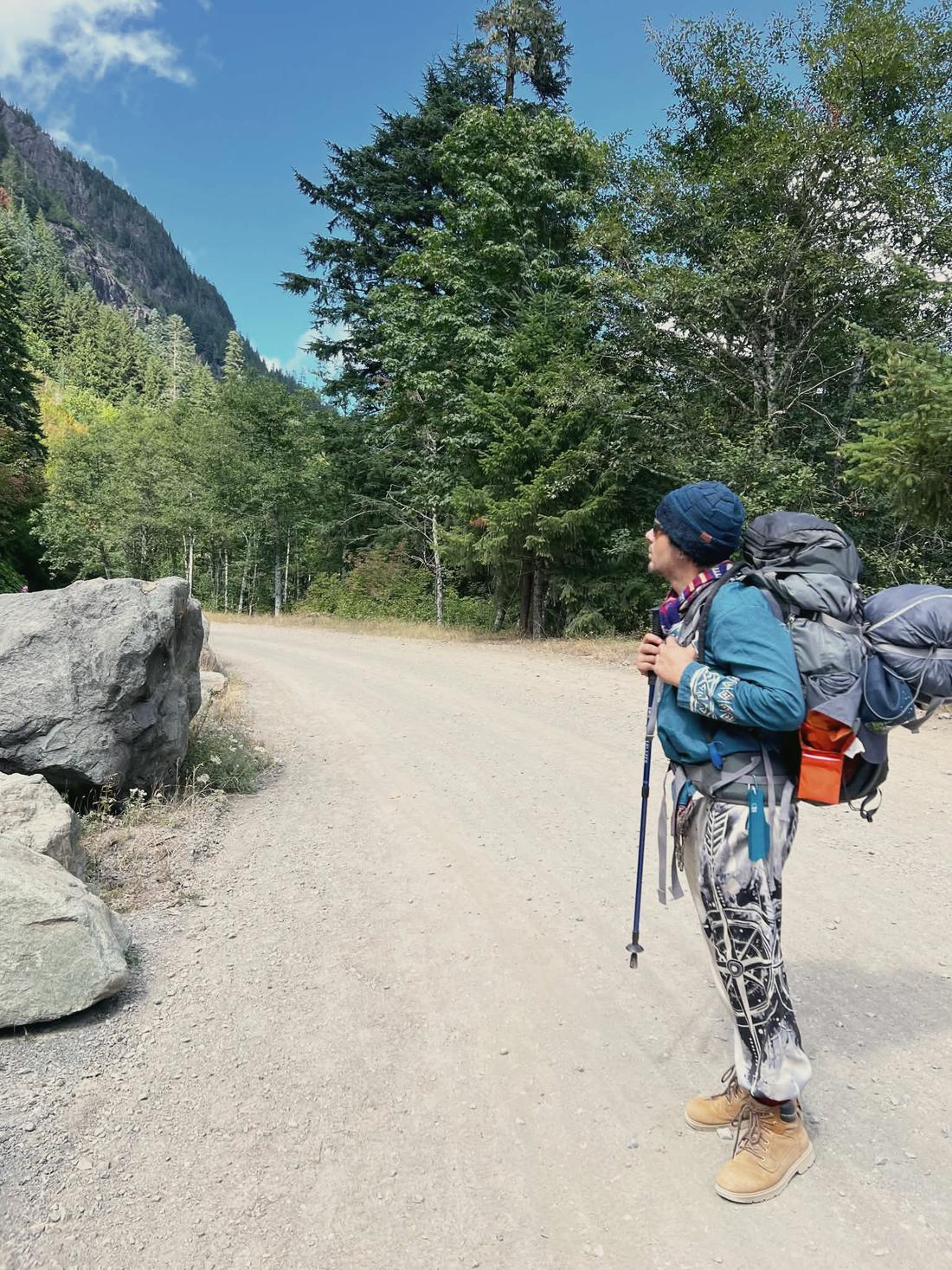 Elijah with a loaded backpack on a gravel road between mountains