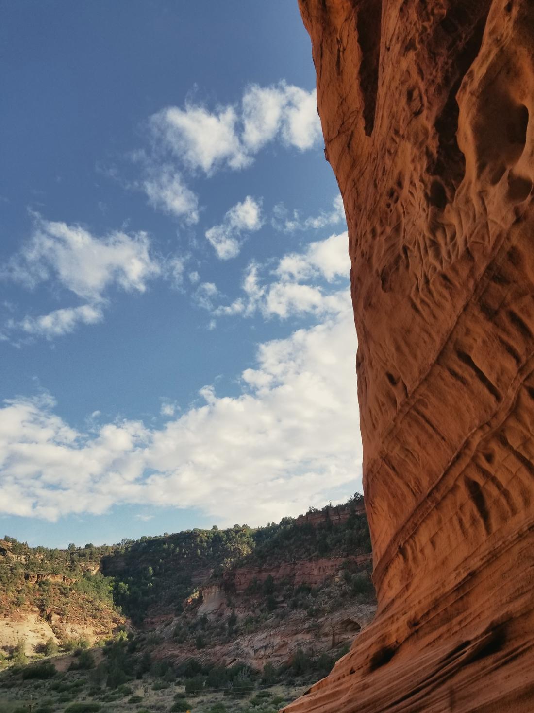 A curved red sandstone wall framing a canyon and a bright sky
