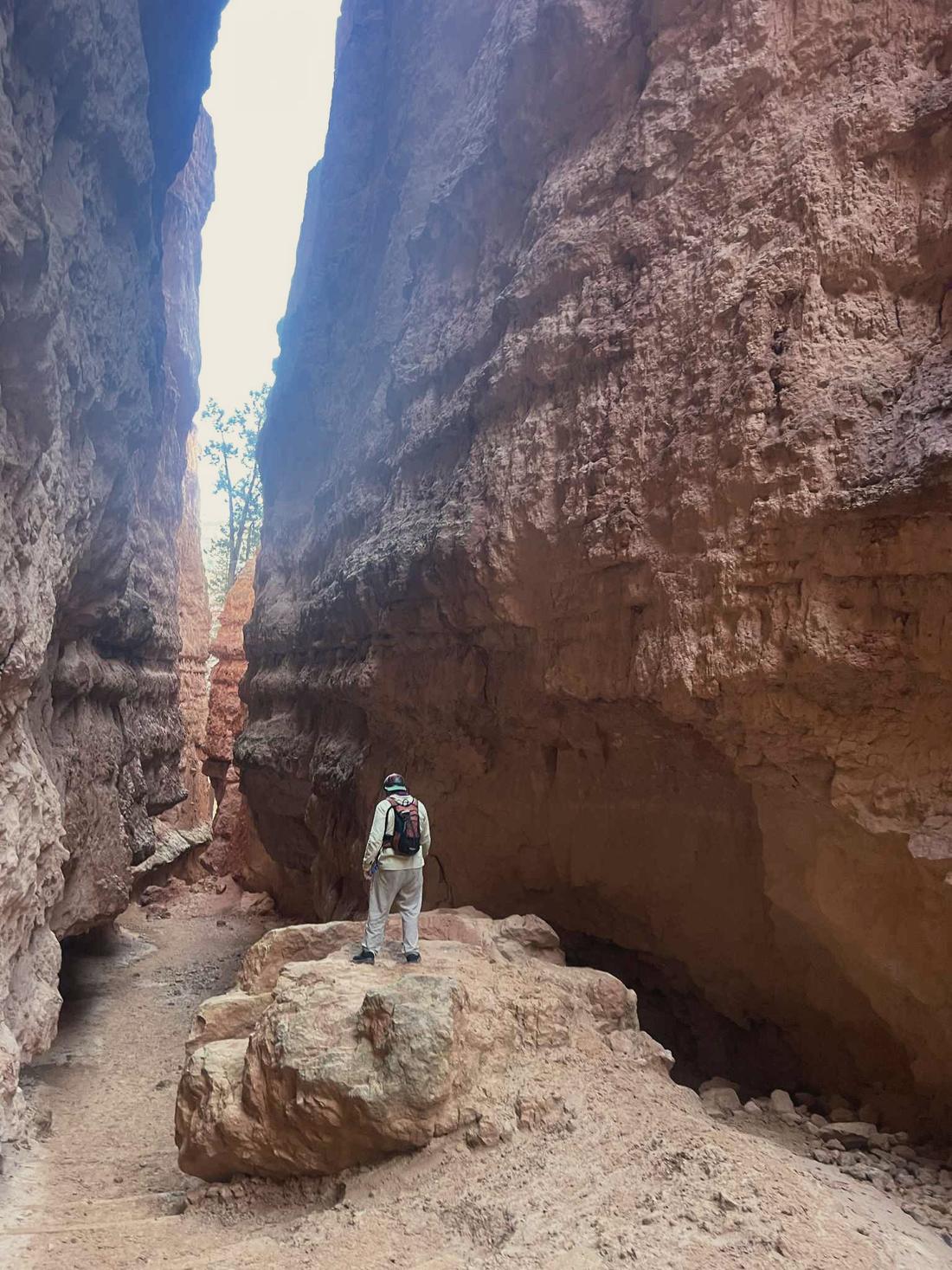 Elijah standing small at the bottom of a narrow red slot canyon