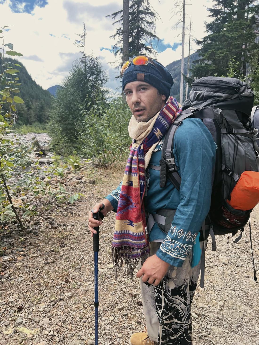 Elijah with a full backpack and trekking poles on a mountain trail