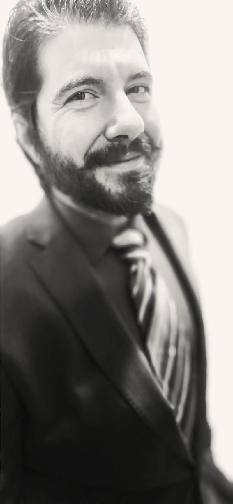 Elijah, founder of Logos & Telos, smiling in a suit and tie, in black and white