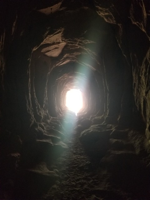 Light pouring in at the end of a narrow sandstone tunnel